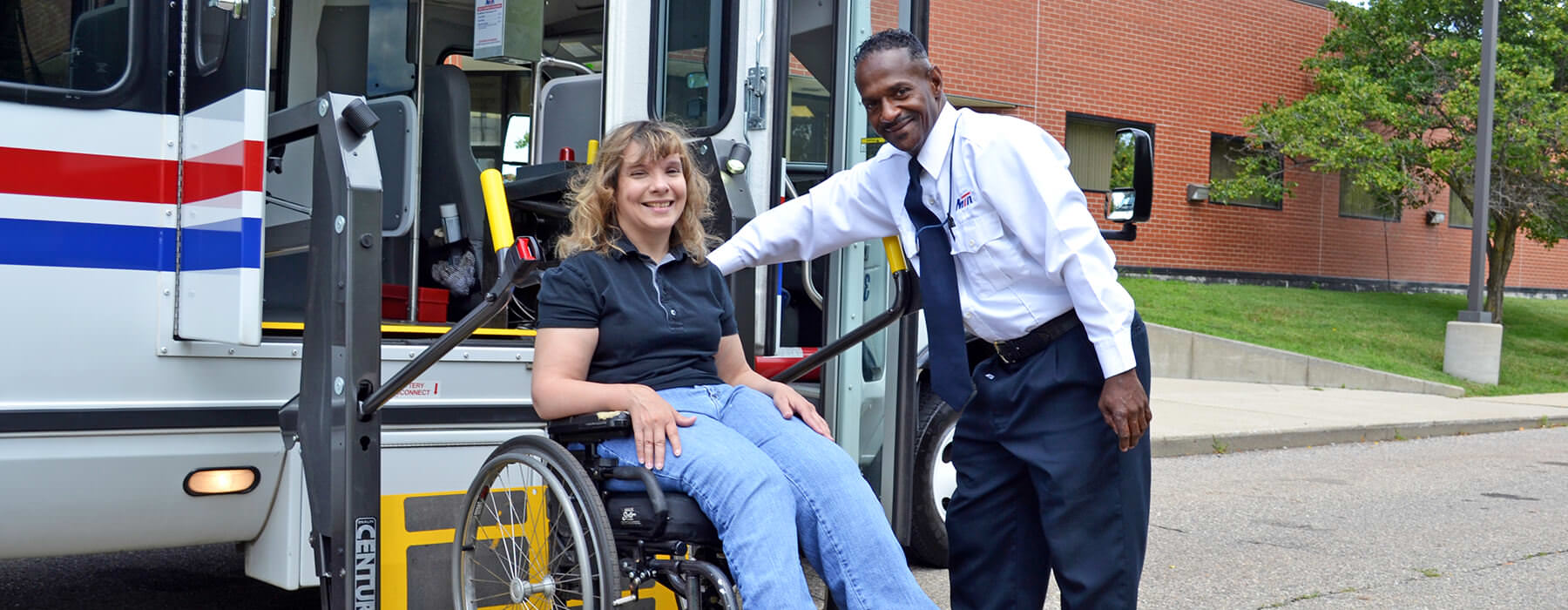 Woman in wheelchair exiting Your Ride bus using the wheelchair lift assisted by the driver.